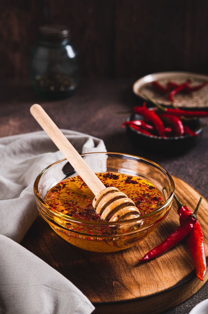 Hot honey in a clear bowl on a table surrounded by red chillies. 