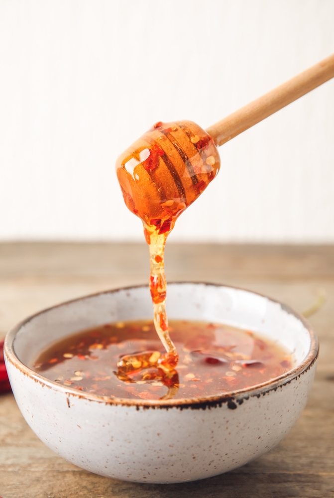 Pouring hot honey from a dipper into a bowl with red chili flakes.