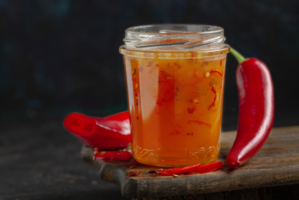 Jar of hot honey and chili peppers on dark background, selective focus. Copy space