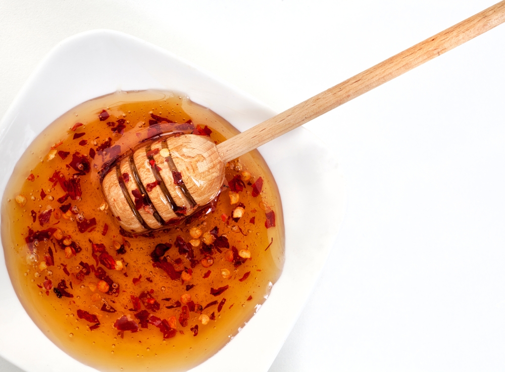 Chili-infused honey in a white bowl surrounded by fresh red peppers.