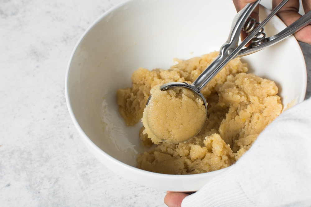 scooping vanilla cookie dough in a white mixing bowl, process of making vanilla cookie dough