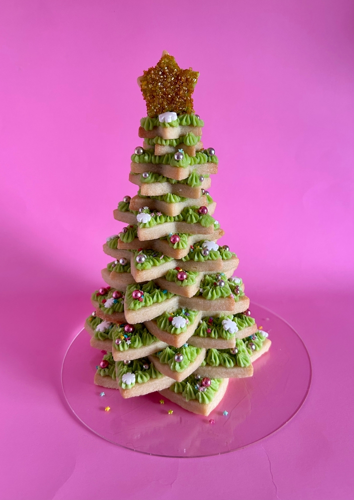 Tree made of stacked sugar cookies with bright green icing on a pink background.
