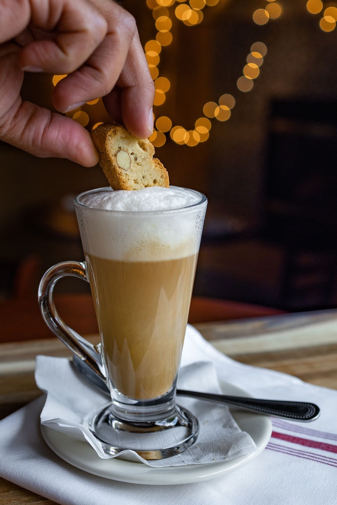 Man's hand dipping biscotti in cappuccino