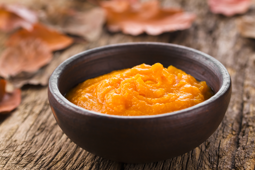 Fresh homemade pumpkin puree in bowl, colorful autumn leaves in the back 