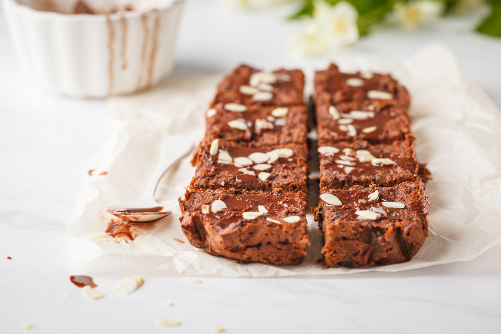vegan brownies on a white plate made from sweet potatoe. There is a spoon next ot then with chocolate sauce on.  