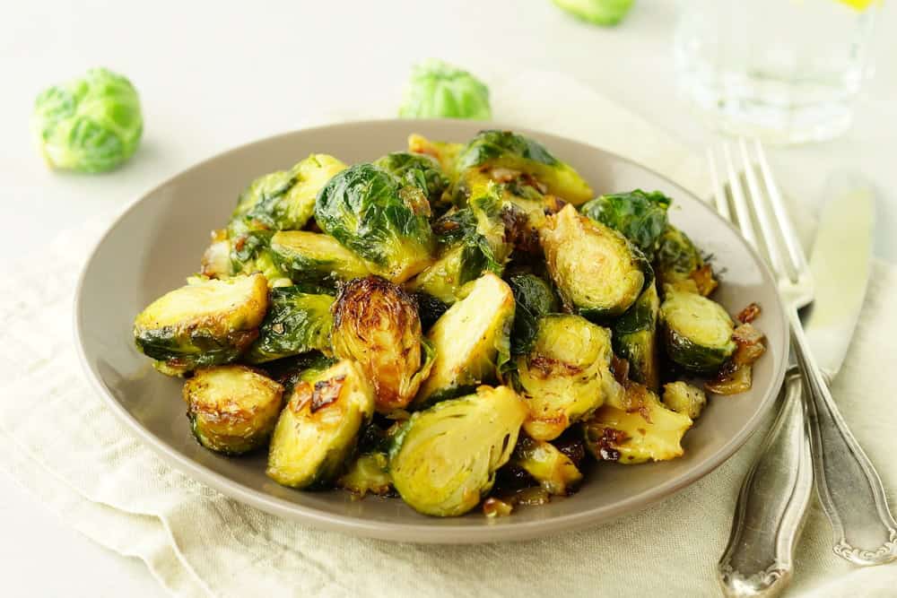 Homemade Roasted Brussel Sprouts with salt, pepper and onions in a beige plate on grey background.