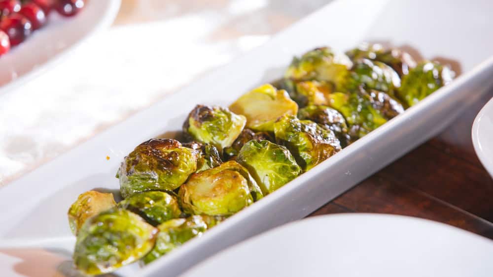 Homemade roasted Brussels sprouts in a long white dish. Garnished with balsamic vinaigrette. Flavorful vegetable makes a perfect side dish for Thanksgiving or Christmas feast. Selective focus. The article is a vegan brussels sprouts recipe.