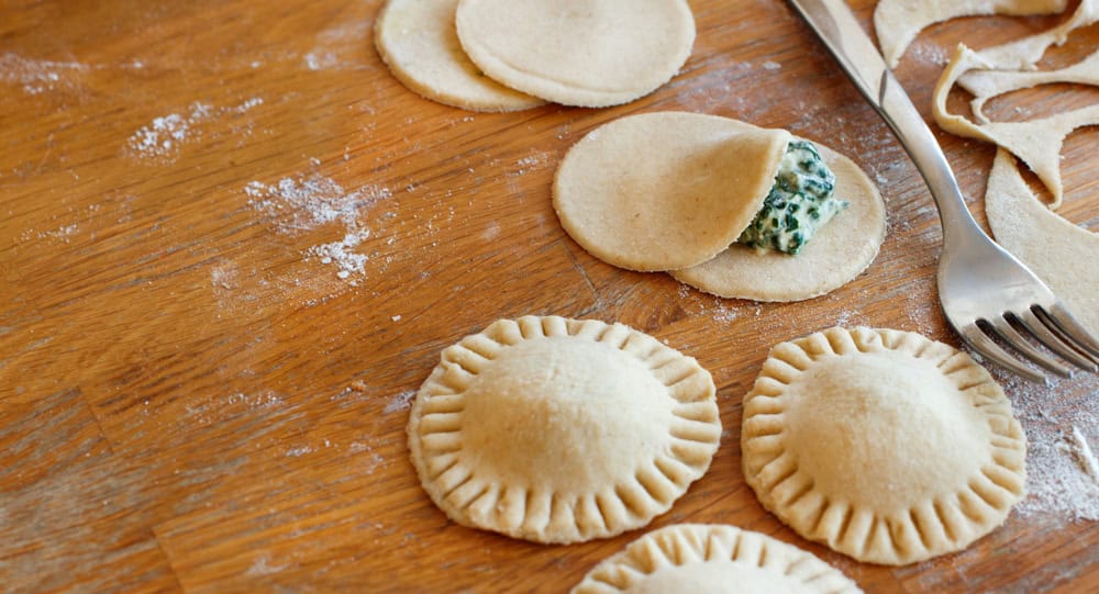 Making ravioli with ricotta cheese and spinach on a wooden board. the article is a ravioli vegan recipe.