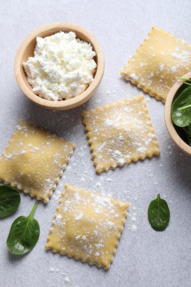 Uncooked ravioli, cheese and spinach on light table, flat lay. It is covered in flour.